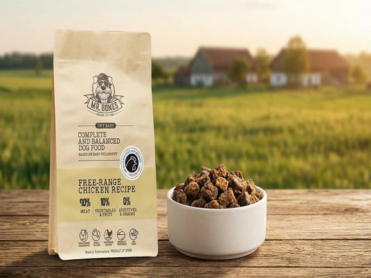 Saco de comida natural Mr. Bones Dry Barf receta de pollo de corral junto a un cuenco con trozos de carne deshidratada en entorno natural.